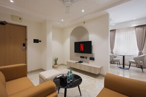 Een moderne woonkamer met een flatscreen televisie aan de muur, een salontafel met waterflesjes en een zithoek met banken.