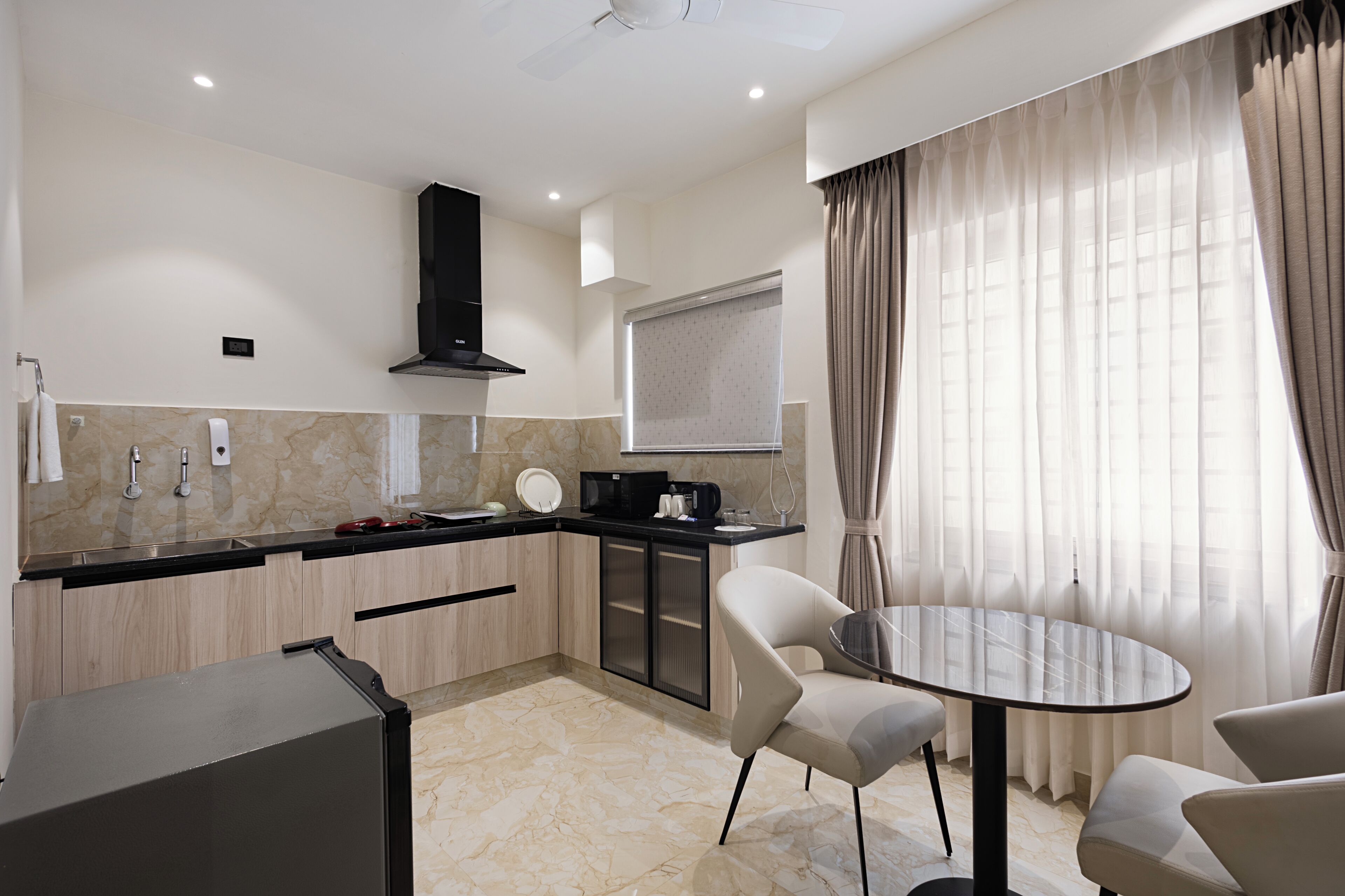 A modern kitchen with a built-in stove, microwave, and black range hood. There is a dining area with a round table and two chairs.