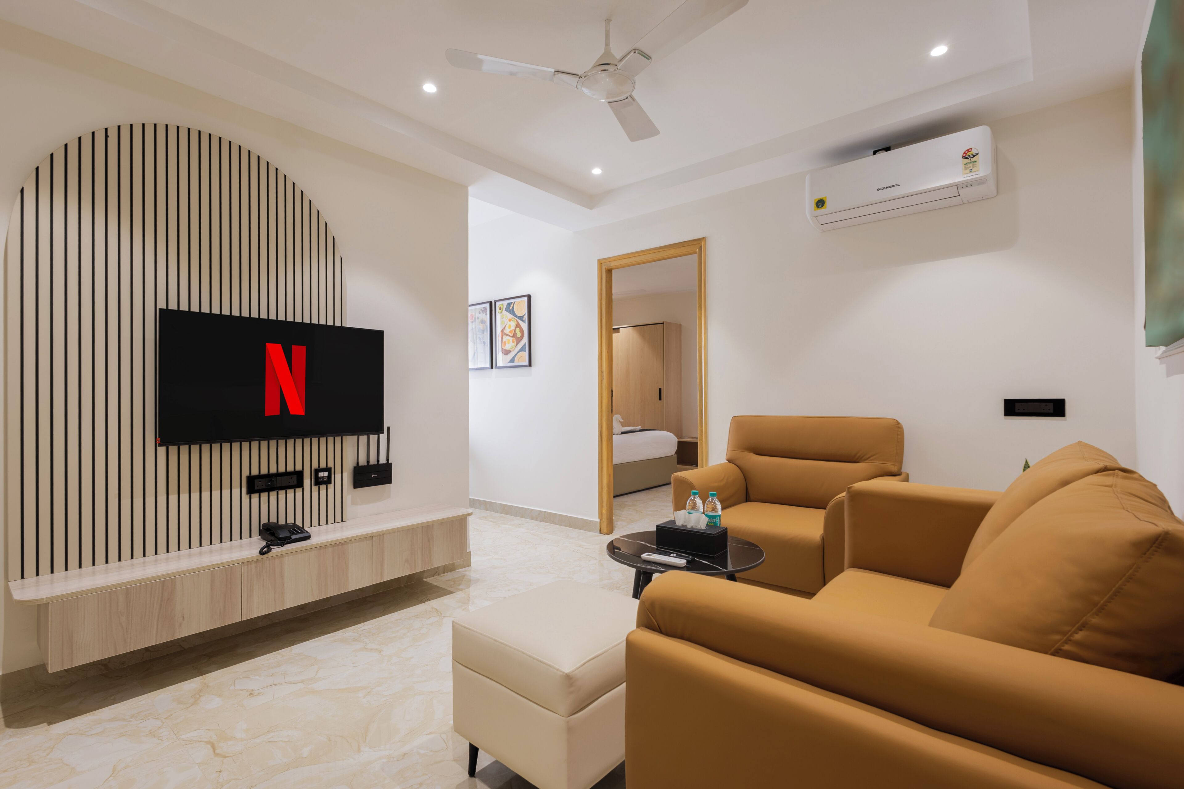 A modern living room with a flat-screen TV mounted on a wall, a ceiling fan, and a sofa.