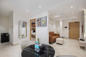 Une chambre d’hôtel moderne avec un sol en marbre, un coin repas doté d’une table en marbre noir, un canapé marron et une porte en bois.