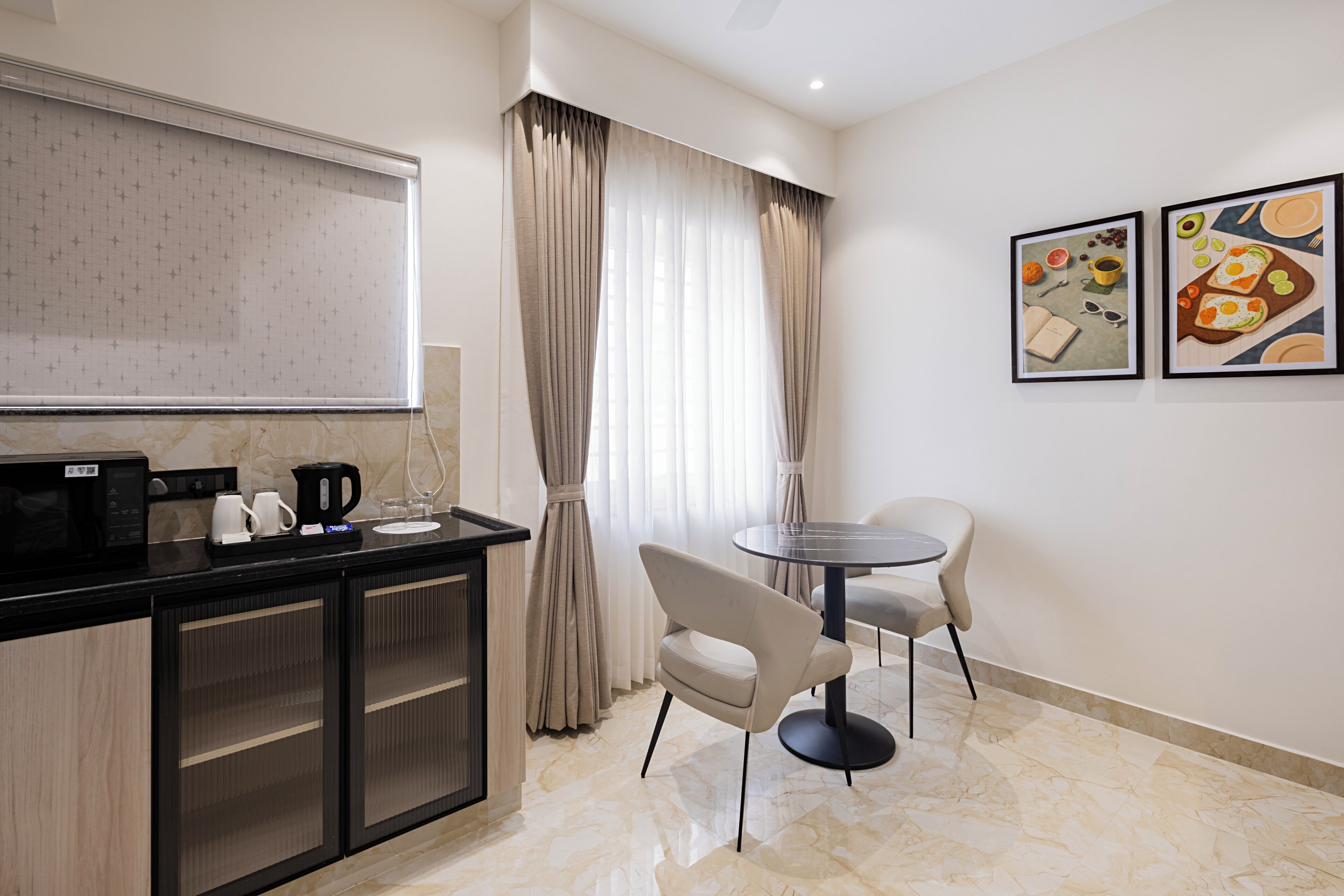 A modern kitchen with a black countertop, a coffee machine, and a microwave. There is a dining area with a round table and two chairs.