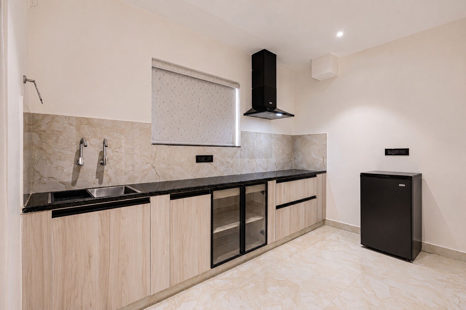 A modern kitchen with a black countertop, wooden cabinets, a stainless steel sink, and a black refrigerator.