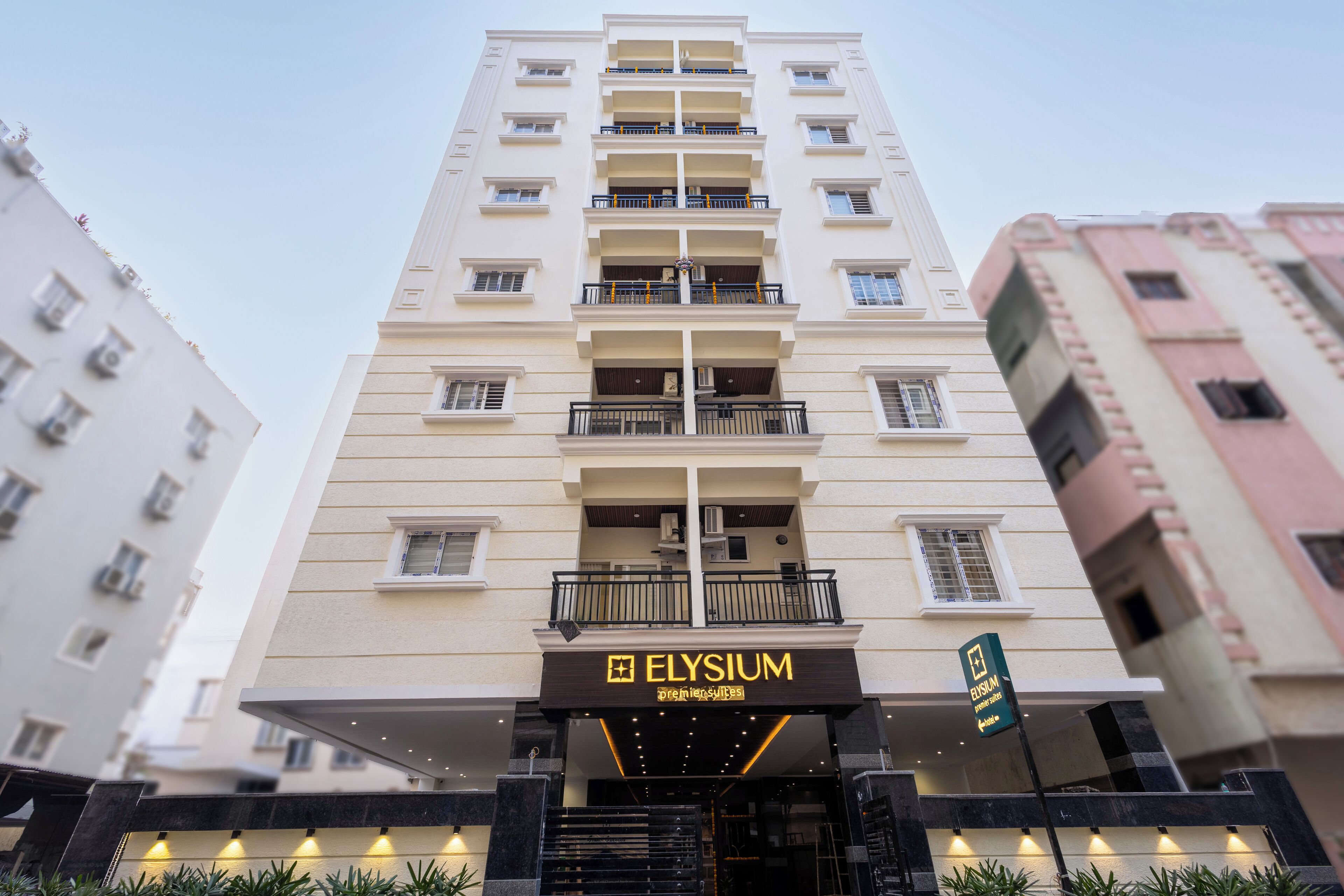 A multi-story hotel named ELYSIUM with a modern facade, multiple balconies, and a prominent entrance with a sign.