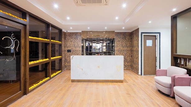 A reception area with a wooden reception desk, a glass partition with yellow flowers, and a seating area with pink chairs.