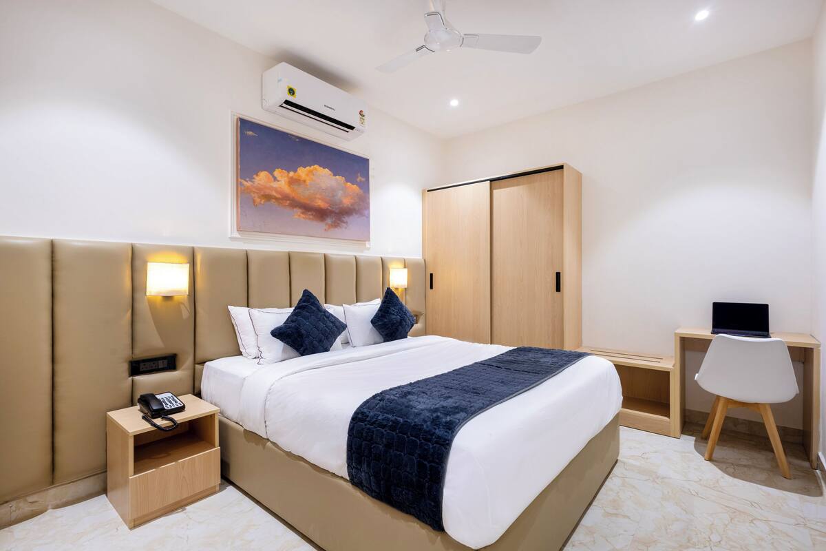 Una habitación de hotel moderna con una cama grande, lámparas de noche, un escritorio con una computadora portátil y un armario.