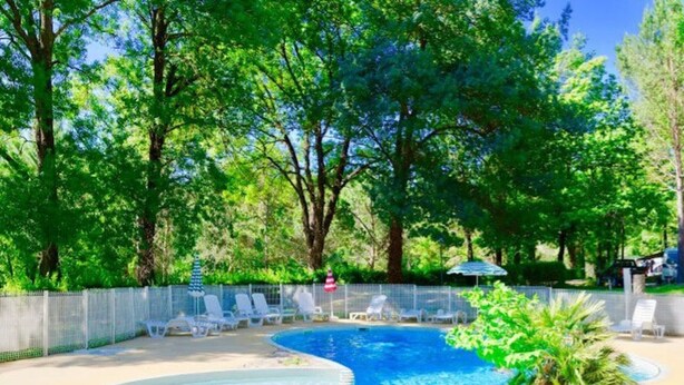 A swimming pool with a curved edge, surrounded by a fence and trees. - Mobile home 3 bedrooms for 6 people with garden furniture (Les Aires)