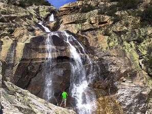 Ein Wasserfall stürzt über eine felsige Klippe, eine Person steht am Fuße.
