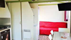 Una cuina compacta amb fogó, nevera blanca i un sofà vermell a la zona de menjador.