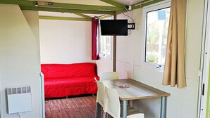 Habitació compacta amb un sofà vermell, una taula petita i un televisor fixat a la paret.