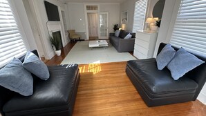 Ein modernes Wohnzimmer mit zwei schwarzen Ledersofas, einem weißen Couchtisch und einem grauen Sofa. In der Ecke steht ein weißes Sideboard und eine Pflanze.