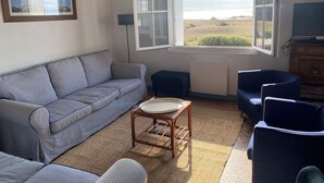 Een woonkamer met een gestreept bankje, een klein rond tafeltje en uitzicht op een wateroppervlak door een groot raam.