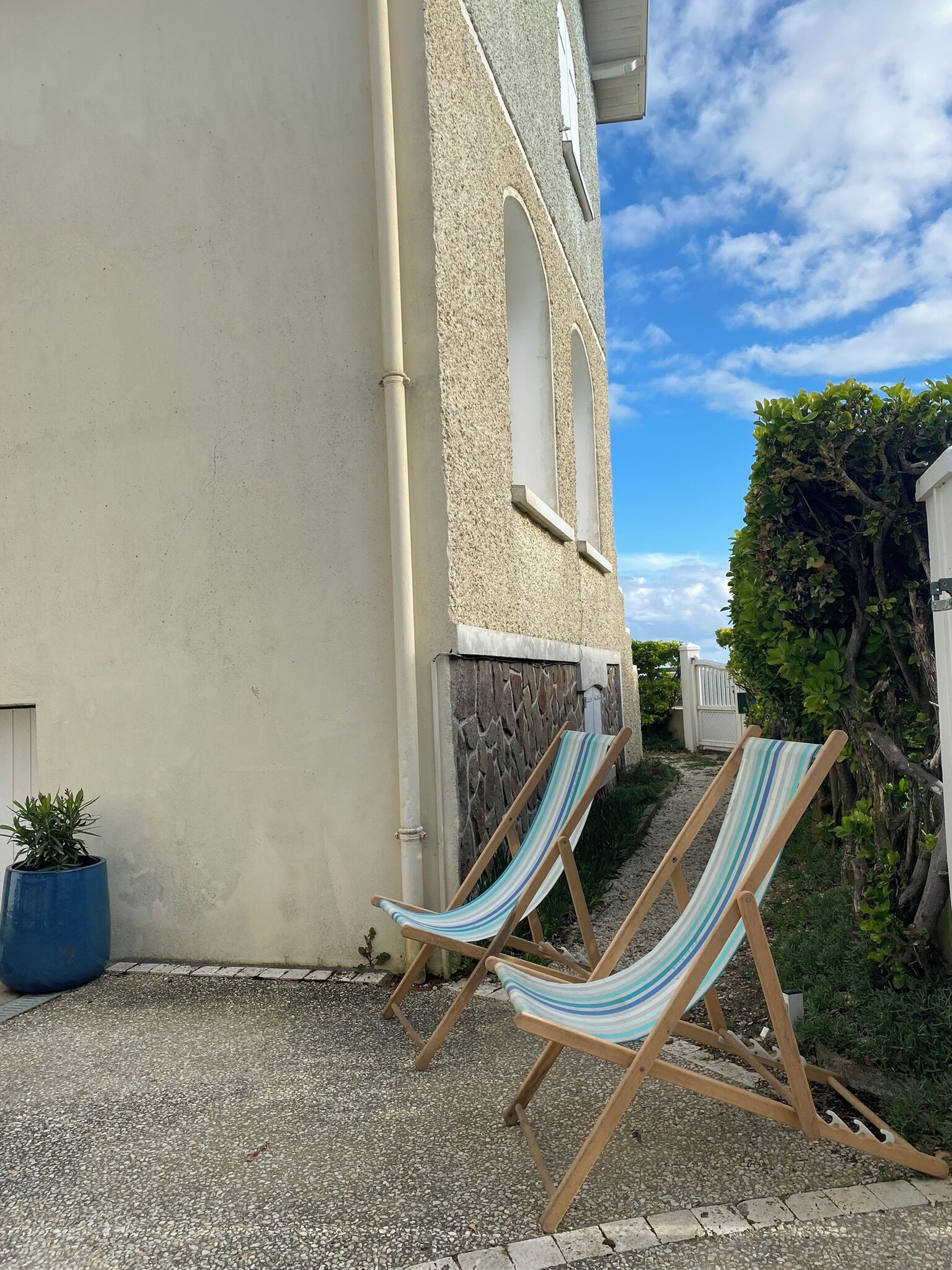 Un bâtiment à la façade en pierre, un chemin de gravier et deux chaises de plage à rayures.