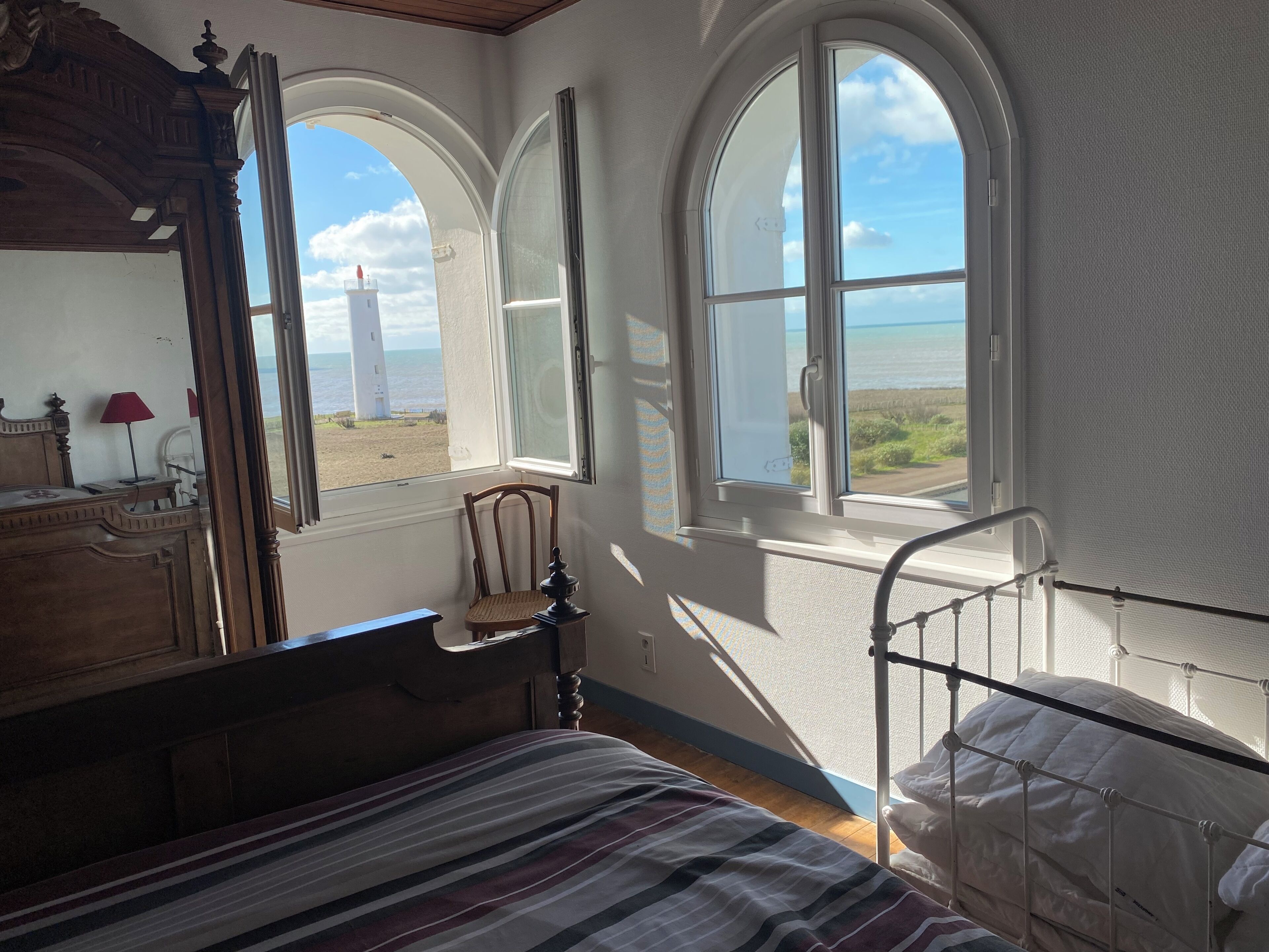 Une chambre à coucher comprenant un lit, une chaise, une commode et deux fenêtres donnant sur la plage.