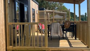 Een houten terras met een tafel en stoelen, een overdekte zithoek en uitzicht op de omgeving.