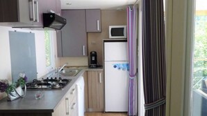 A compact kitchen with a gas stove, microwave, and refrigerator. - Mobile-home 4 pers with bedrooms & garden furniture (Champagnac-le-Vieux)
