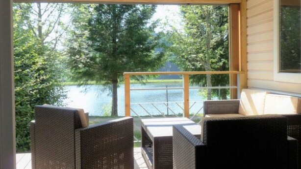 A covered outdoor seating area with wicker furniture, overlooking a lake. - Mobile-home 4 pers with bedrooms & garden furniture (Champagnac-le-Vieux)