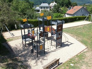 Une aire de jeux dotée d’une structure ludique sur le thème d’un château, comprenant des toboggans et des filets d’escalade, entourée d’une zone sablonneuse avec un banc à proximité.