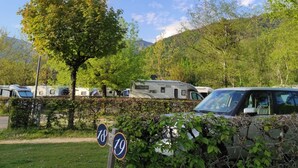 Een camping met campers en een auto, omgeven door bomen en heuvels.