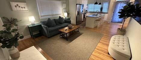 Una sala de estar moderna con un sofá gris, una mesa de centro de madera y un ventanal con persianas.