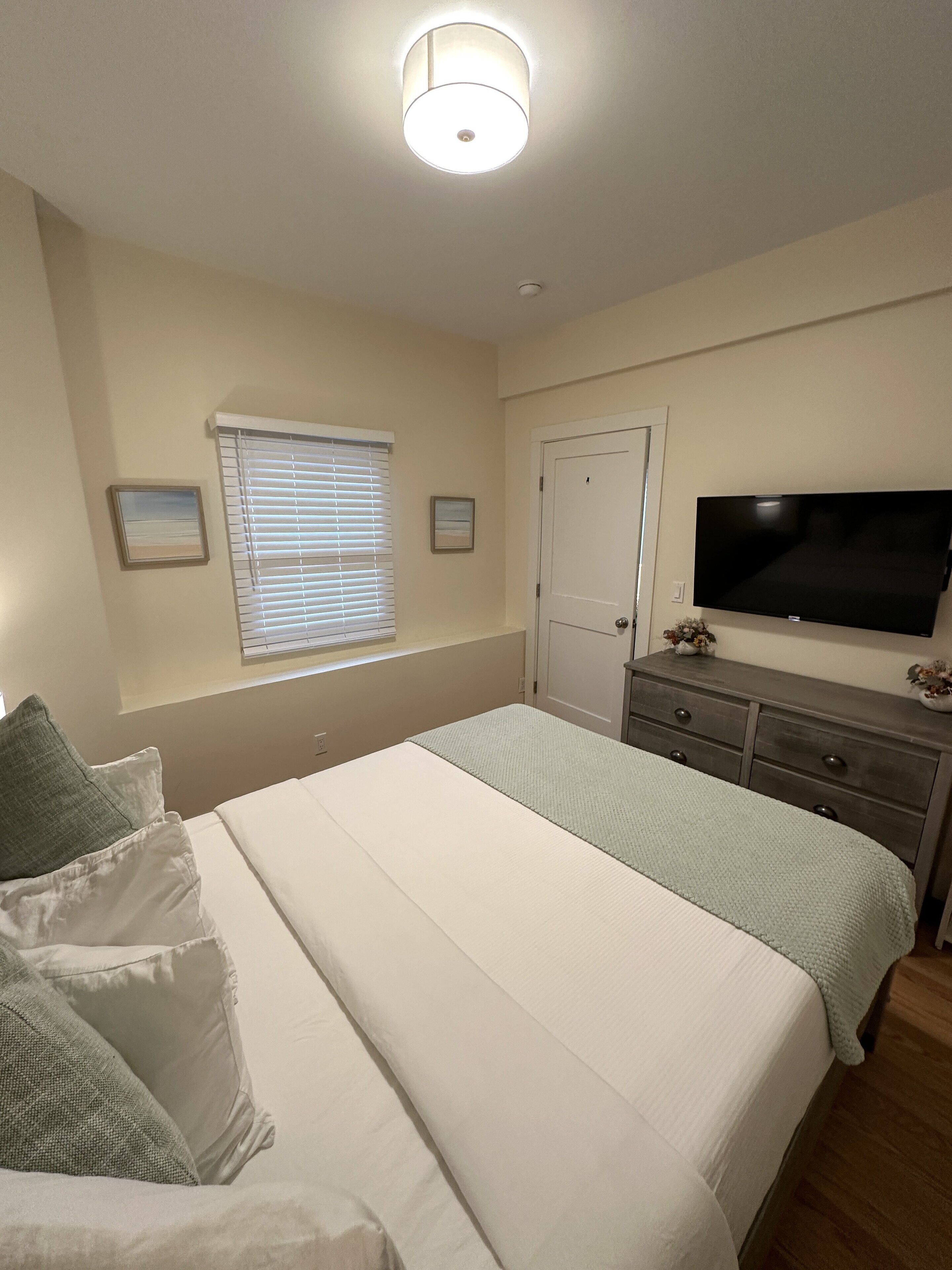 Un dormitorio con cama, cómoda, televisor y ventana con persianas.