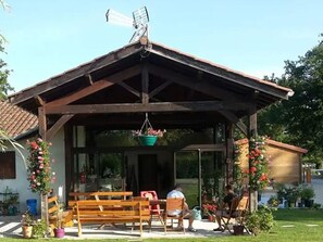 A covered outdoor seating area with benches and hanging flower baskets. - Mobile home with terrace for 6 people (Sandrans)