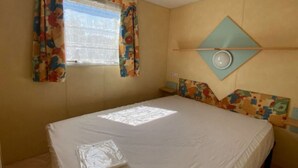 Un dormitorio con una cama, una ventana con cortinas, un espejo redondo sujeto a la pared y un cabecero colorido.