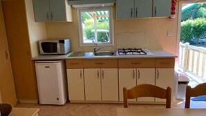 Cocina compacta con microondas, pileta y estufa. Una ventana ofrece luz natural y vista a plantas verdes.