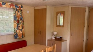 Una habitación compacta con una mesa de madera, un banco rojo, una pequeña cocina americana con cafetera y un espejo sobre la puerta.