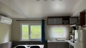 Cozinha compacta com mesa e cadeiras, janela com vista para área verde e micro-ondas.