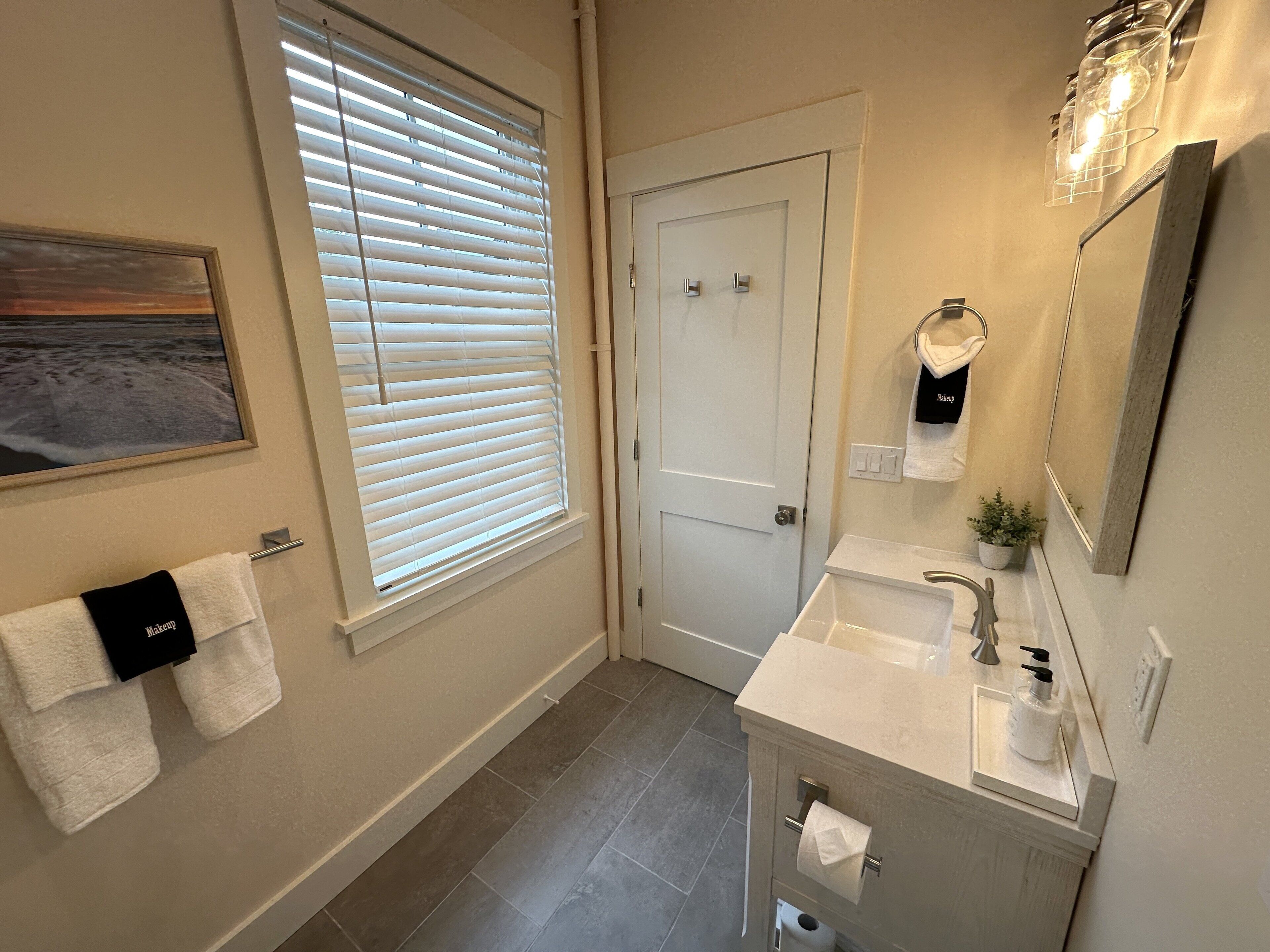 Une salle de bain équipée d’un lavabo, d’un miroir, d’un porte-serviettes et d’une fenêtre avec des stores.
