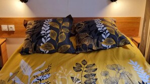Ein Bett mit floraler Tagesdecke und zwei Kissen mit Blätermotiv.