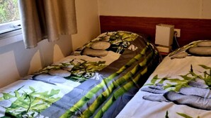 Ein Schlafzimmer mit zwei Einzelbetten, einem Fenster mit Vorhang, einem Wandlautsprecher und einem gerahmten Bild über den Betten.
