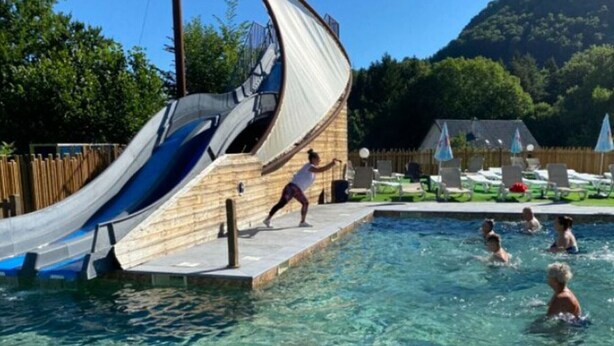 A swimming pool with a slide, surrounded by lounge chairs and umbrellas. - Mobile Home 4 pers with Terrace in Vic-sur-Cère (Vic-sur-Cère)