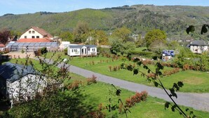 A rural setting with a house, a greenhouse, and a path leading through a green landscape. - Mobile Home 4 pers with Terrace in Vic-sur-Cère (Vic-sur-Cère)