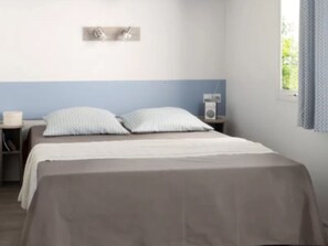 A bedroom with a bed, bedside tables, a wall-mounted light, and a window with curtains. - Spacious mobile home 6 pers with terrace (Sandrans)