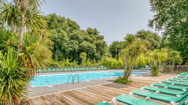 A pool area with wooden decking, green lounge chairs, and a clear blue pool surrounded by lush greenery. - Mobile Home for 6, Spacious Terrace (Saint-Paul-en-Born)