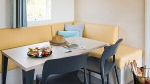 A corner dining area with a table set for two, a hat, and a basket of fruit on the table. - Mobile Home for 6, Spacious Terrace (Saint-Paul-en-Born)