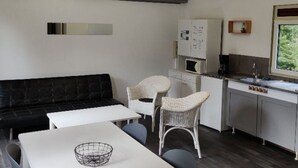 Ein gemütlicher Wohnraum mit Sofa, Esstisch, zwei Stühlen, einer Küchenzeile mit Spüle und einem Fenster mit Blick ins Grüne.