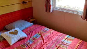 Ein Schlafzimmer mit einem Holzkopfende, einem Bett mit farbenfroher Steudecke, einem Kissen mit Herzmuster und einem Fenster mit Vorhängen.