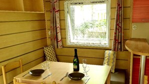 Ein Essbereich mit einem Tisch für zwei Personen, einer Weinflasche und einem Fenster mit Vorhängen.