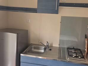 Eine kleine Küche mit einem Edelstahlkühlschrank, einer Spüle und einem Gasherd.