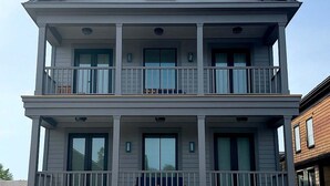 A two-story residential building with a balcony on each floor, large windows, and a wooden fence in front. - Brand New! 2 Bed W/ Private Deck 2 Bedroom Apts (Newport)