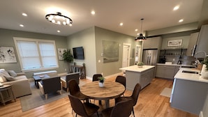 A modern kitchen with a dining area, wooden flooring, and a central island. - Brand New! 2 Bed W/ Private Deck 2 Bedroom Apts (Newport)