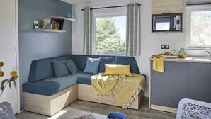 A modern, compact living space with a built-in sofa, a small kitchen area, and a large window providing natural light. - 3-Bedroom Mobile Home with Terrace in Saint-Julien-en-Born (Saint-Julien-en-Born)
