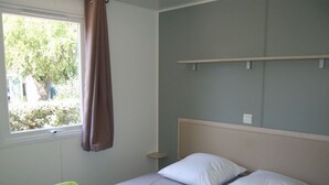 A bedroom with a bed, a window with curtains, a bedside table, and a wall-mounted shelf. - Mobile home 3 bedrooms in Cavaillon with terrace (Cavaillon)