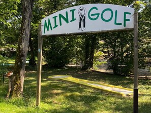 A sign for a mini golf course with a yellow putting green and a wooden post.