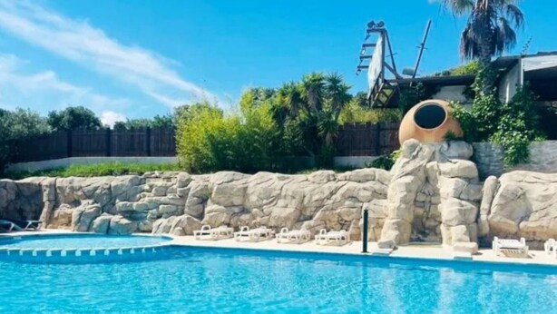 A swimming pool with clear blue water, surrounded by a rocky wall and palm trees. - Mobile Home 5 pers, Terrace at La Rouquette (Calvisson)