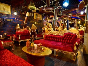 Ein luxuriöser Raum mit aufwändiger Einrichtung, darunter eine rote Samsofa und goldverzierte Stühle sowie ein Holztisch.