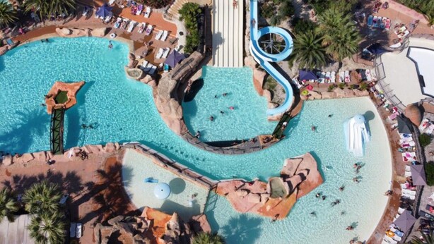 Vista aérea de un complejo turístico con múltiples piscinas, un tobogán acuático y zonas de descanso.
