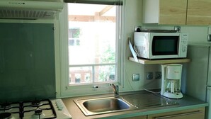 A compact kitchen with a gas stove, a microwave, a coffee maker, and a window with blinds. - Comfortable Mobile Home with Terrace in Collias (Collias)